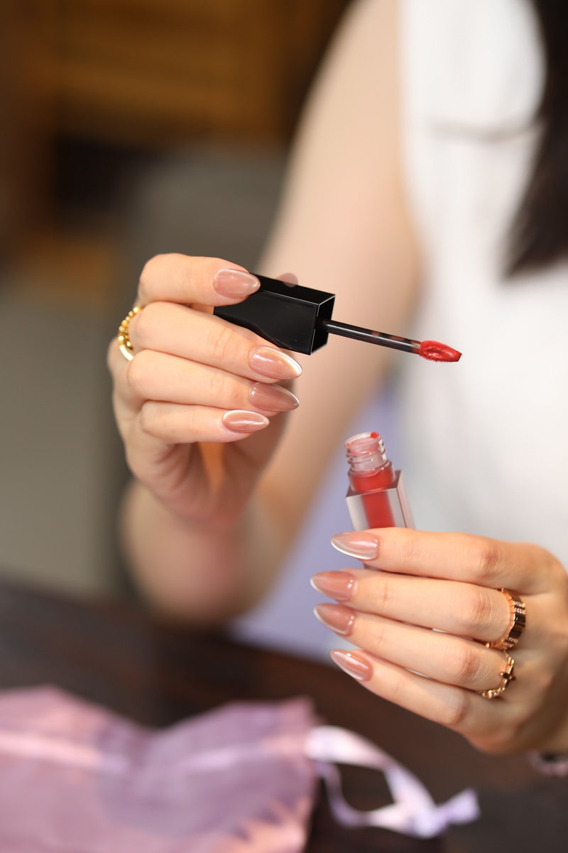 Glossy nude press-on nails holding a lip gloss applicator